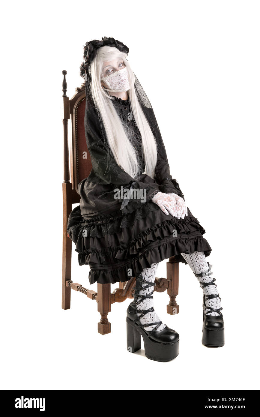 Girl in a black dress with white eyes looking like a doll in a chair isolated in white Stock Photo