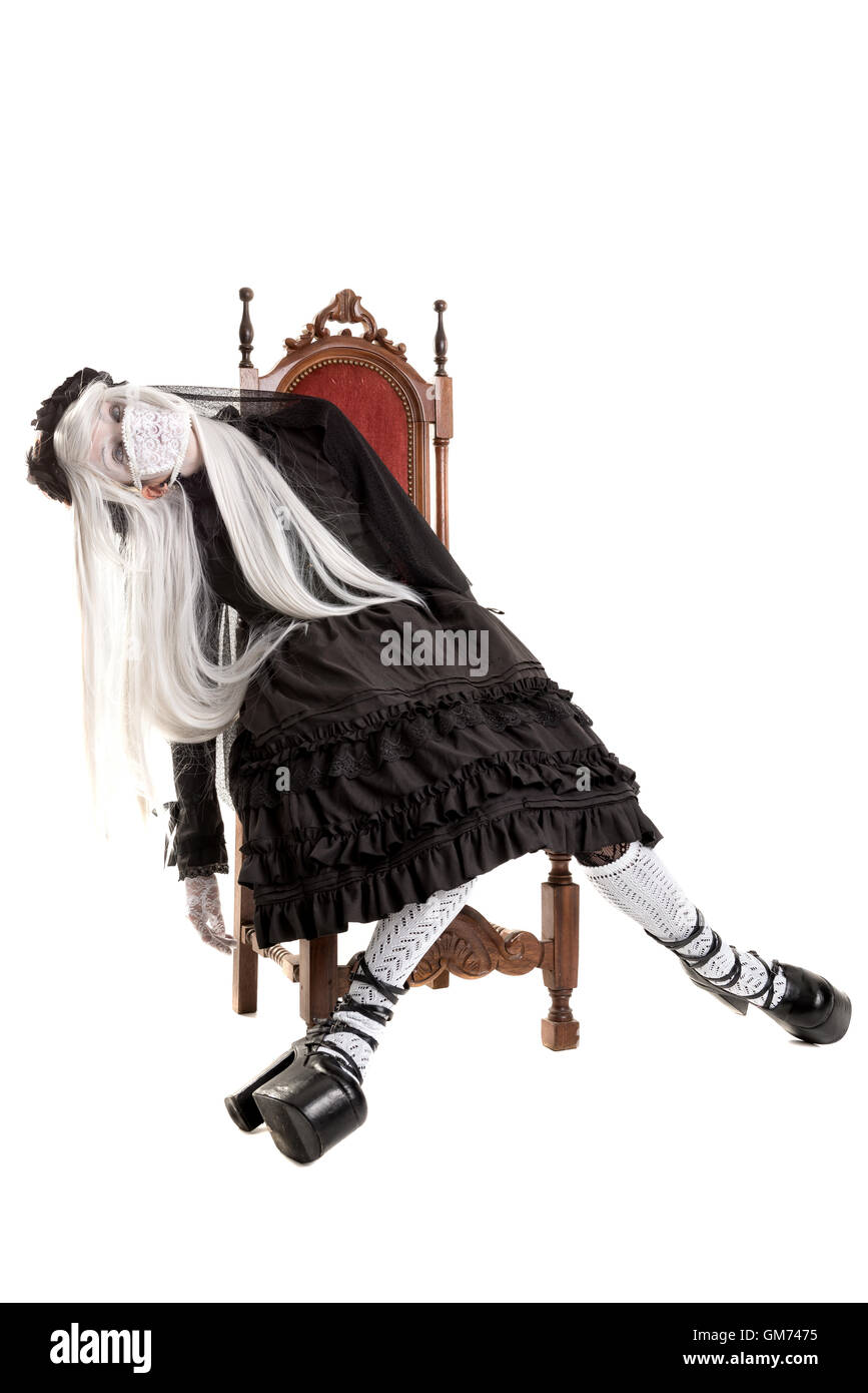 Girl in a black dress with white eyes looking like a doll in a chair isolated in white Stock Photo