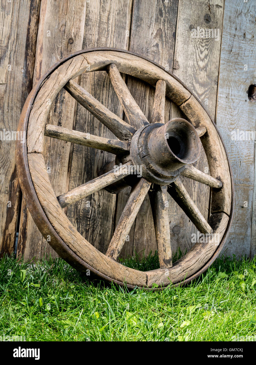 Old wooden wagon wheel resting against rustic wooden fence Stock Photo