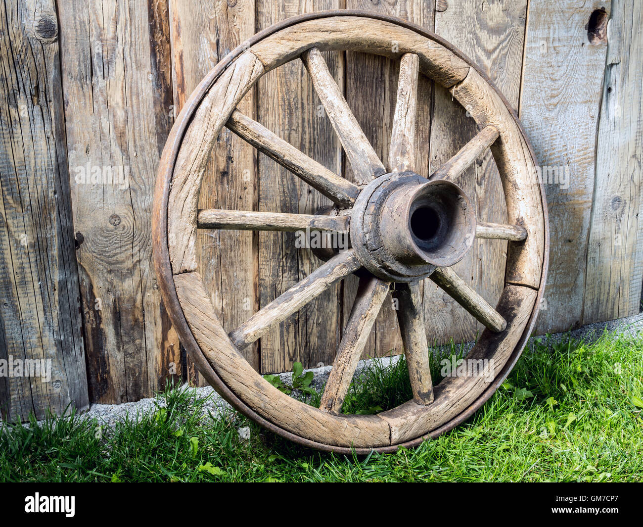 Old wooden wagon wheel resting against rustic wooden fence Stock Photo