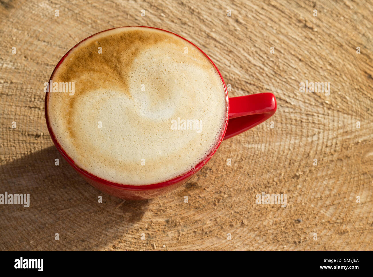 A beautiful cappuccino in golden sunlight sat on a natural piece of wood. Stock Photo