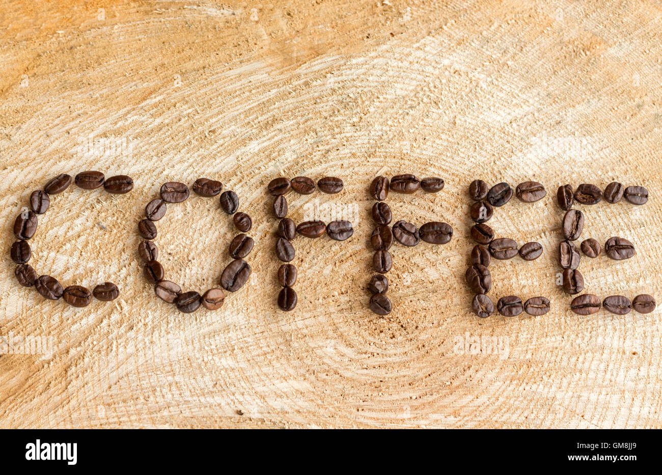 The word Coffee laid out using roasted coffee beans on a natural wood background. Stock Photo