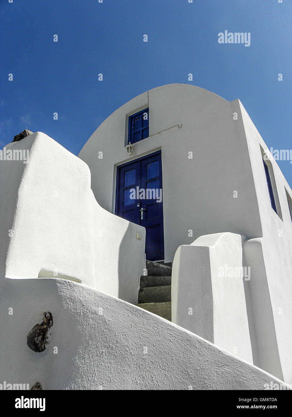 A bright white house with a blue door matches the blue sky Stock Photo ...