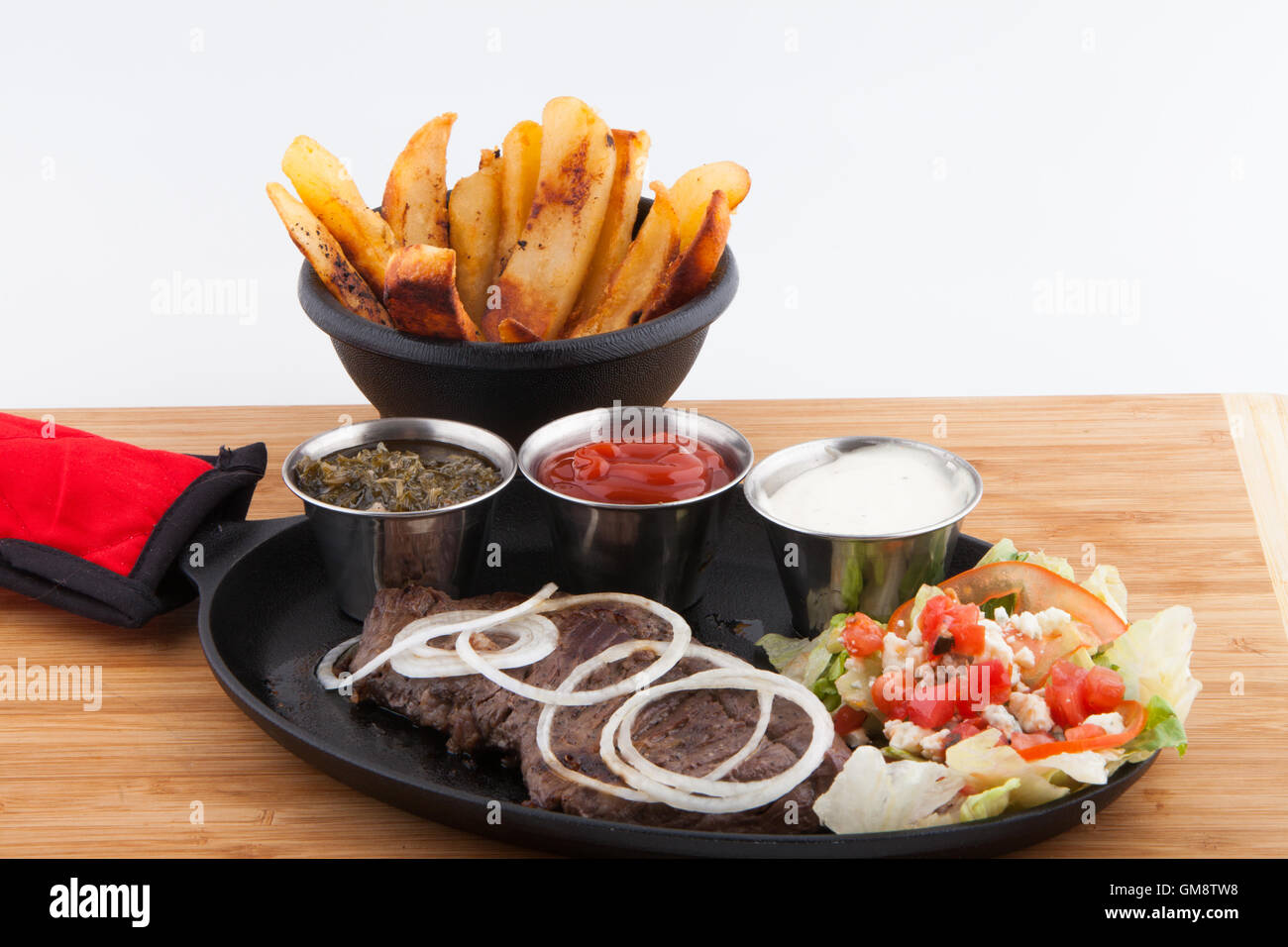 Flank steak,French Fries fresh garnish sauces Ketchup catsup table sauce Ranch dressing, Chimichurri cast iron skillet Stock Photo