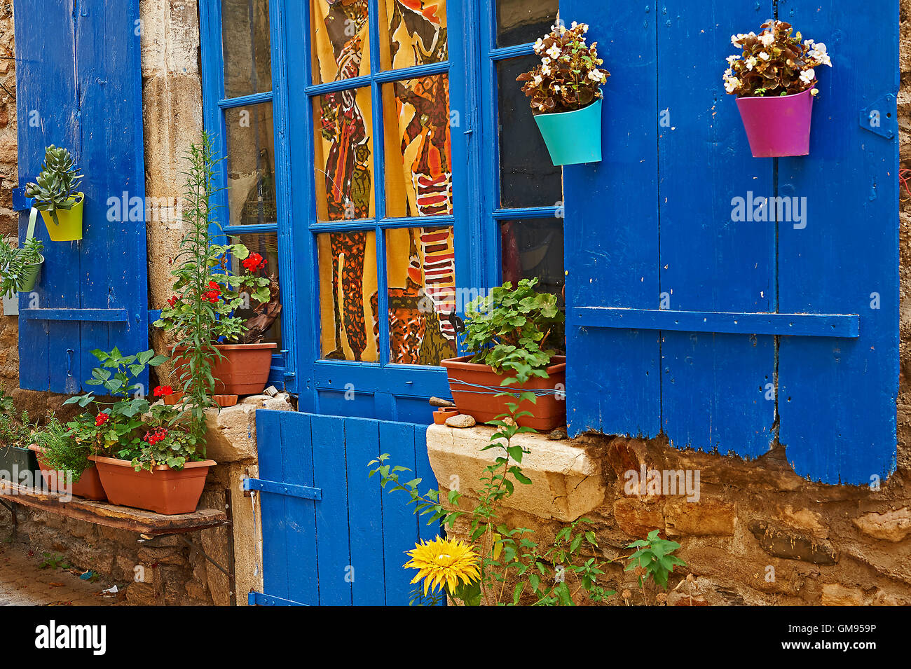 Plant pots and boxes outside a window with blue coloured shutters in the small village of Olargues. Stock Photo