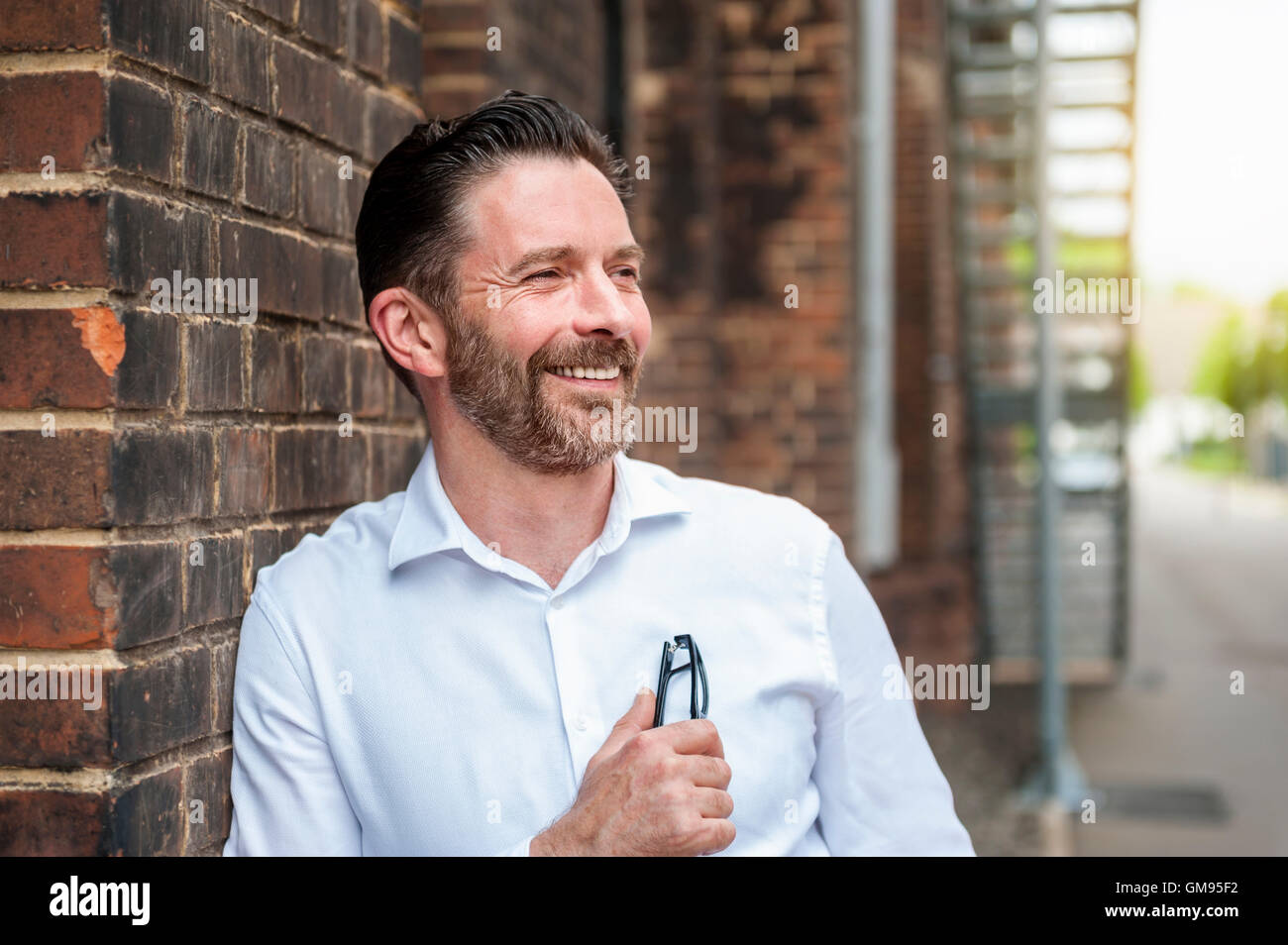 Portrait of smiling businessman leaning at brick wall Stock Photo