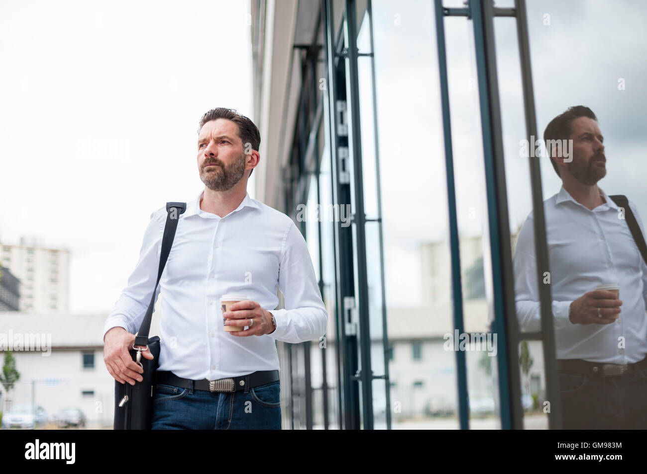 Serious businessman with coffee to go in front of glass facade Stock Photo