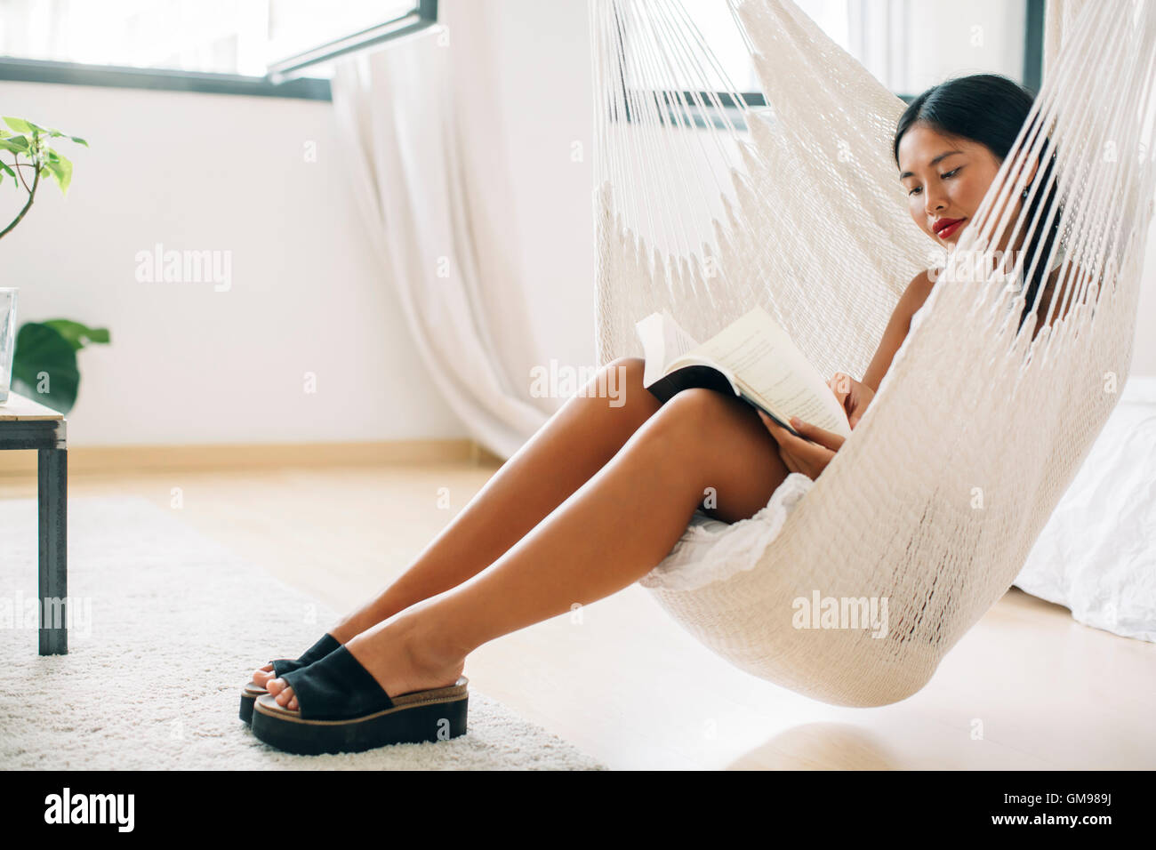 Young woman sitting in hammock reading book Stock Photo - Alamy