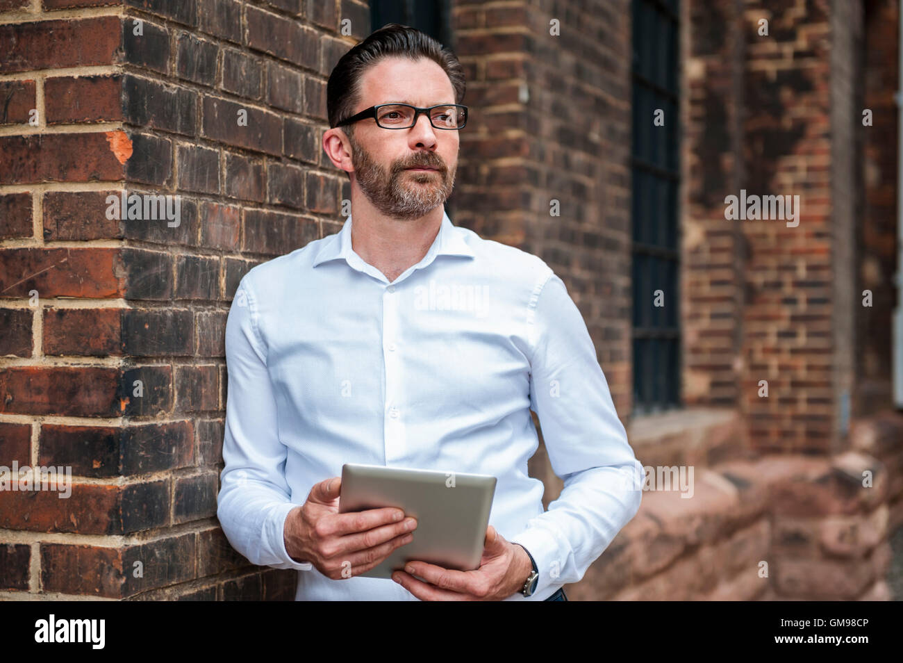 Portrait of businessman with tablet leaning at brick wall Stock Photo