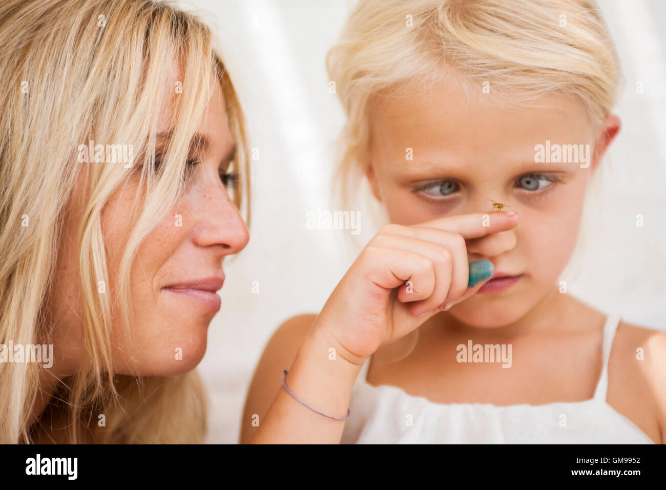 Cross-eyed little girl watching fly sitting on her finger Stock Photo