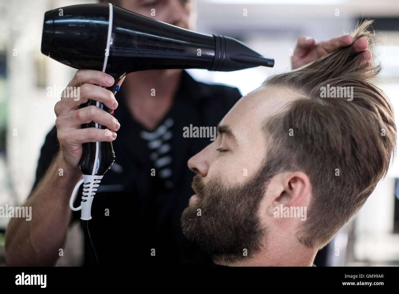 Barber blow-drying hair of a customer Stock Photo - Alamy