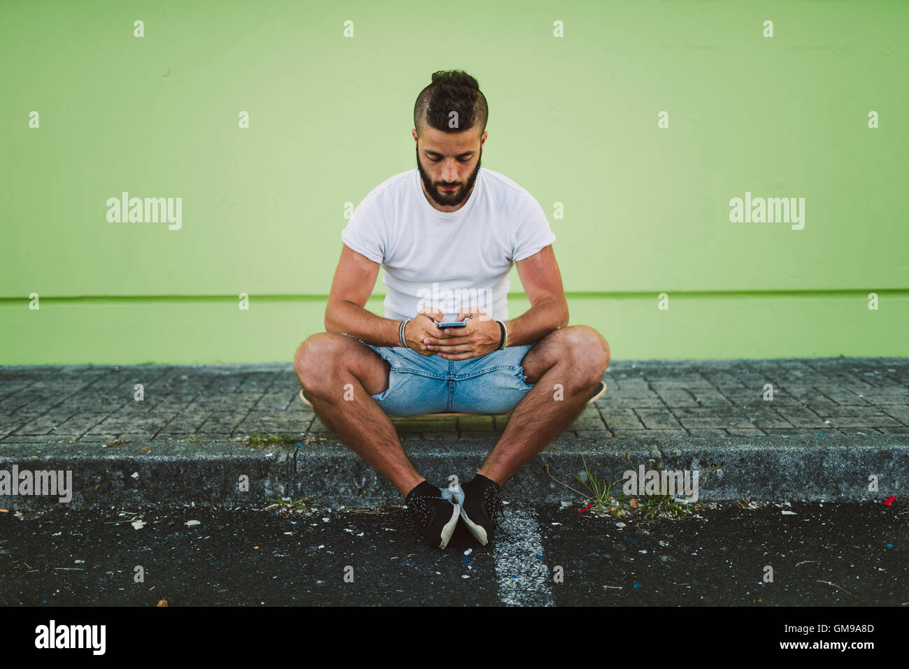 Man sitting on his skateboard at carb text messaging Stock Photo
