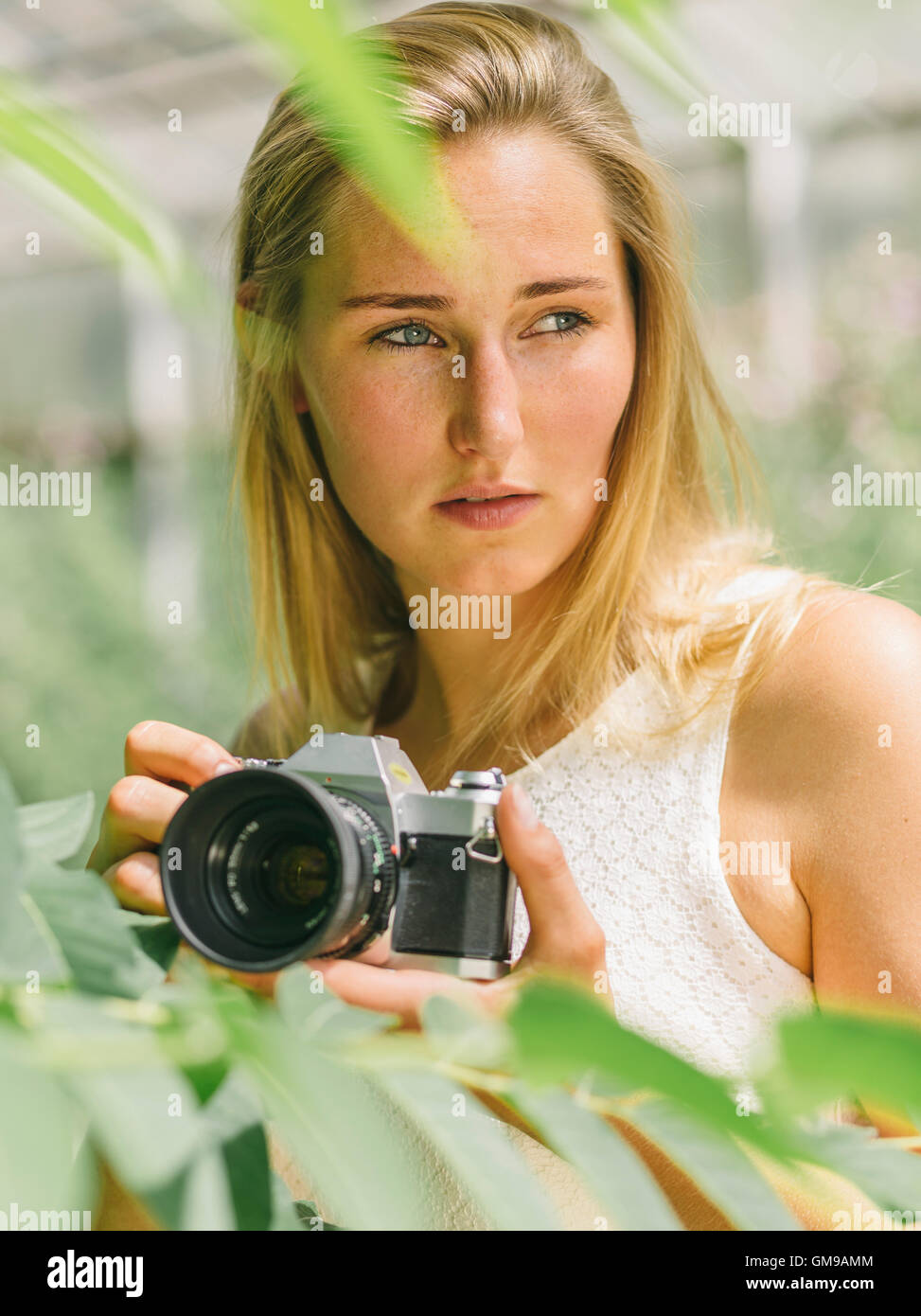 Young woman behind plant holding camera Stock Photo - Alamy