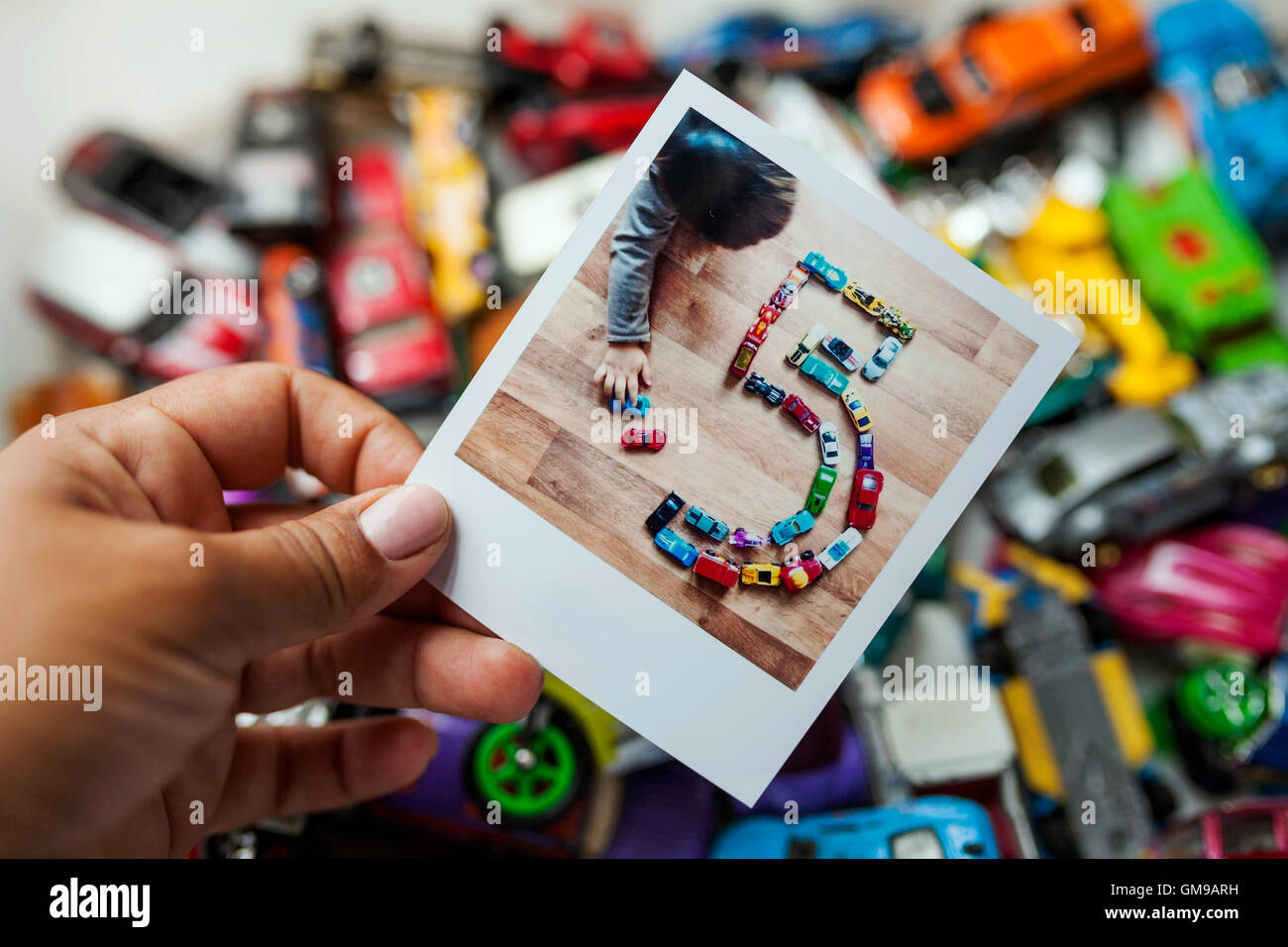 Polaroid of a little kid playing with his cars making a number five Stock Photo