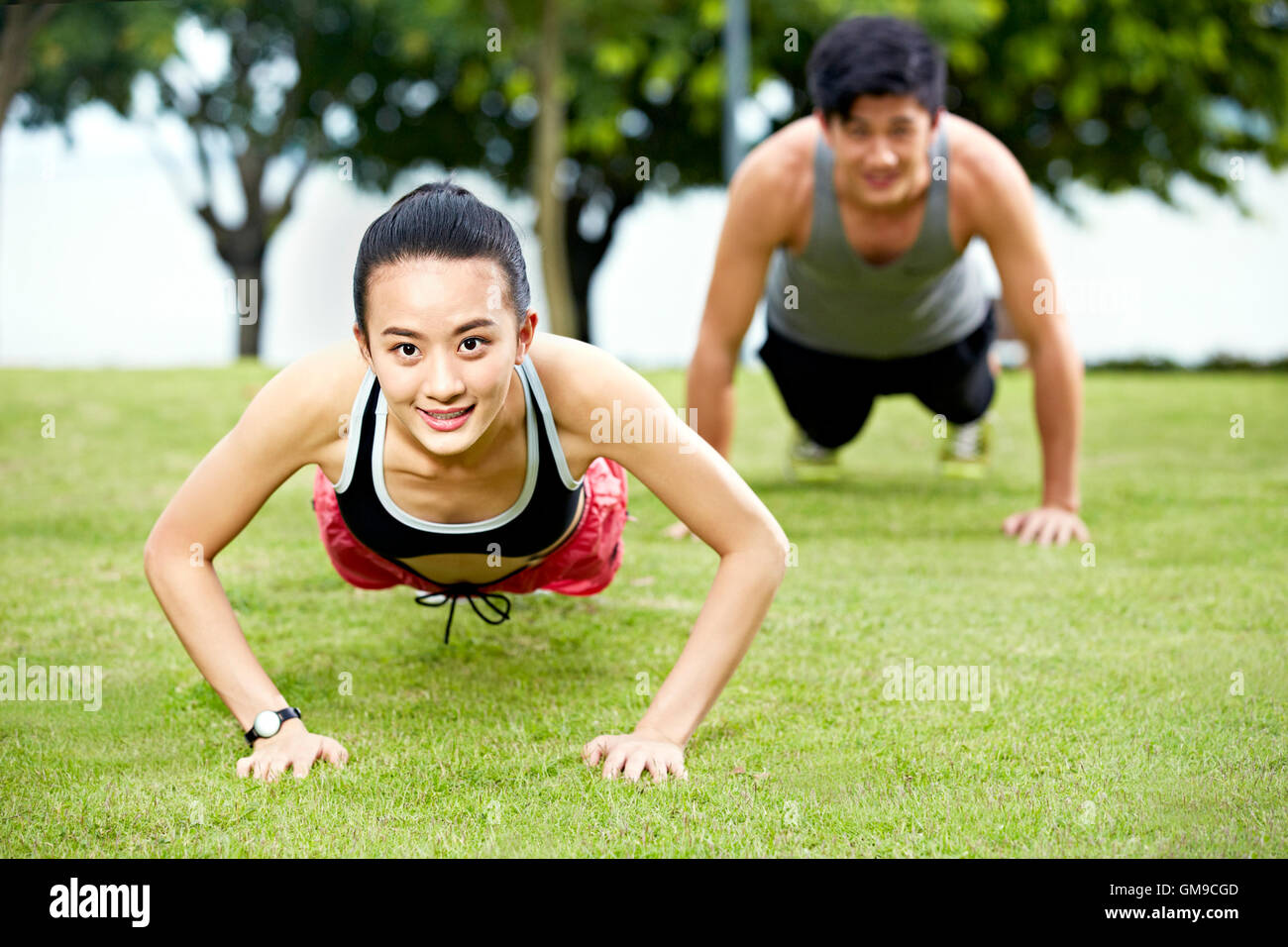 young asian man and woman couple doing push-ups on grass in a city park. Stock Photo