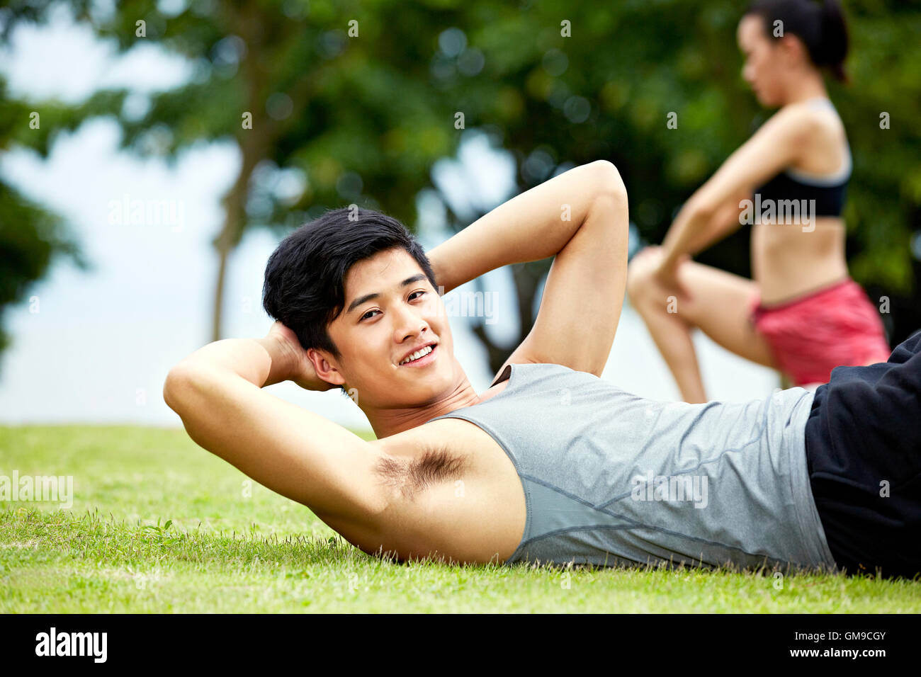 young asian man doing sit-ups on grass in city park. Stock Photo