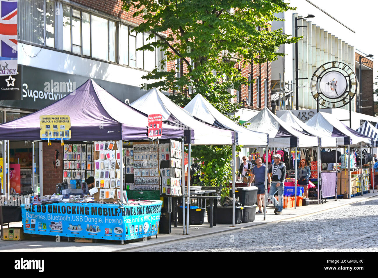 Brentwood Essex England UK High Street shopping and stall holders amongst various market stalls with town clock beyond sunny summer market day Stock Photo