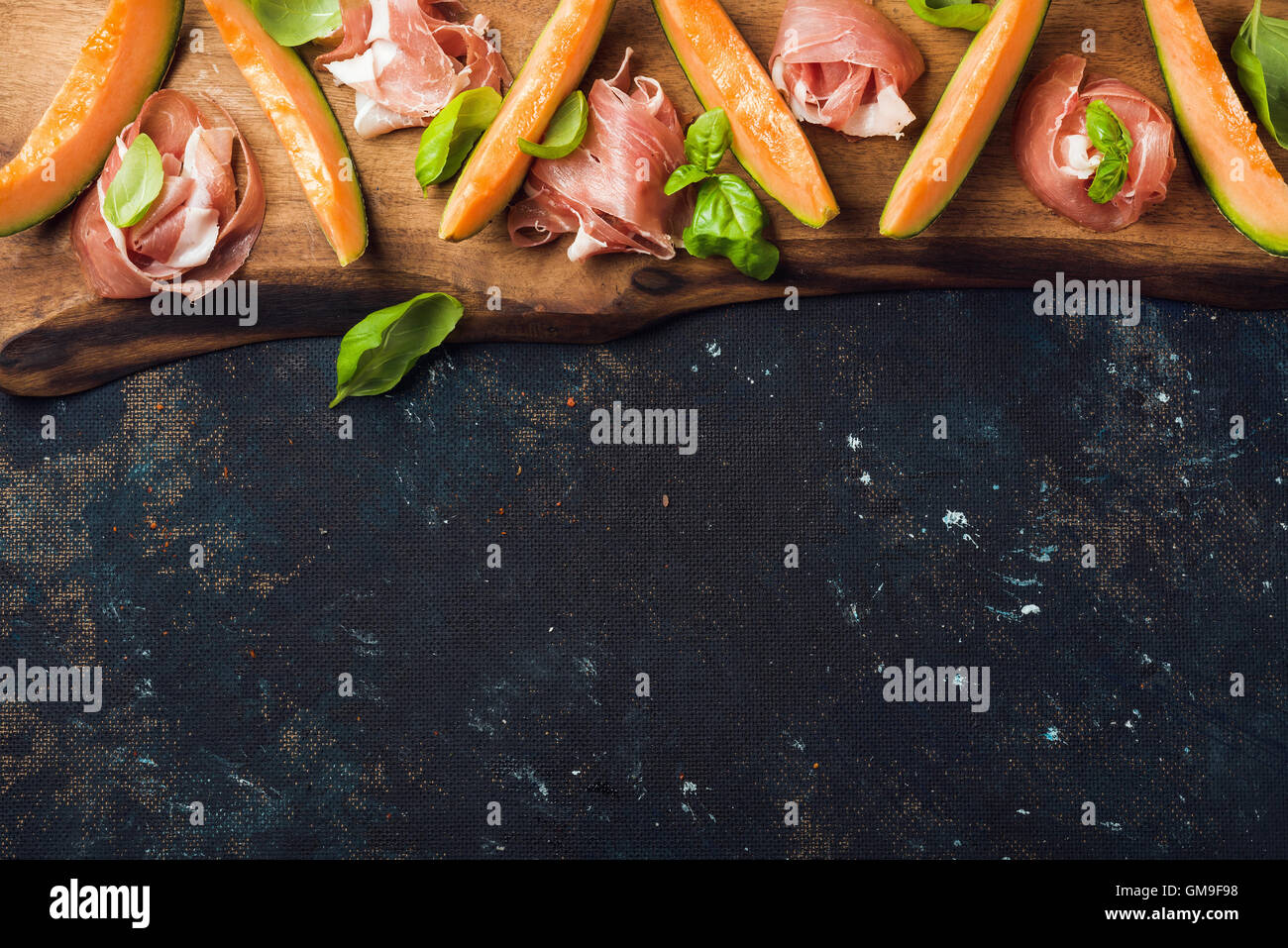 Prosciutto with cantaloupe melon and basil leaves on wooden board Stock