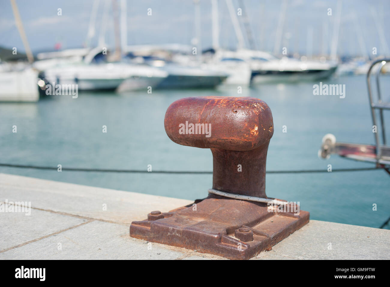 Rusted mooring bollard  in dock of harbor pier,  sailing boat out of focus in background Stock Photo