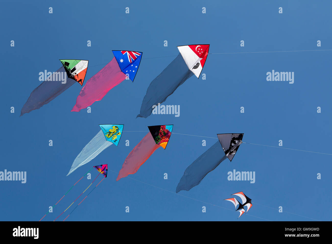 Group of six colourful kites flying in a clear blue sky. Flags and symbols on decorated silk high in the sky. Stock Photo