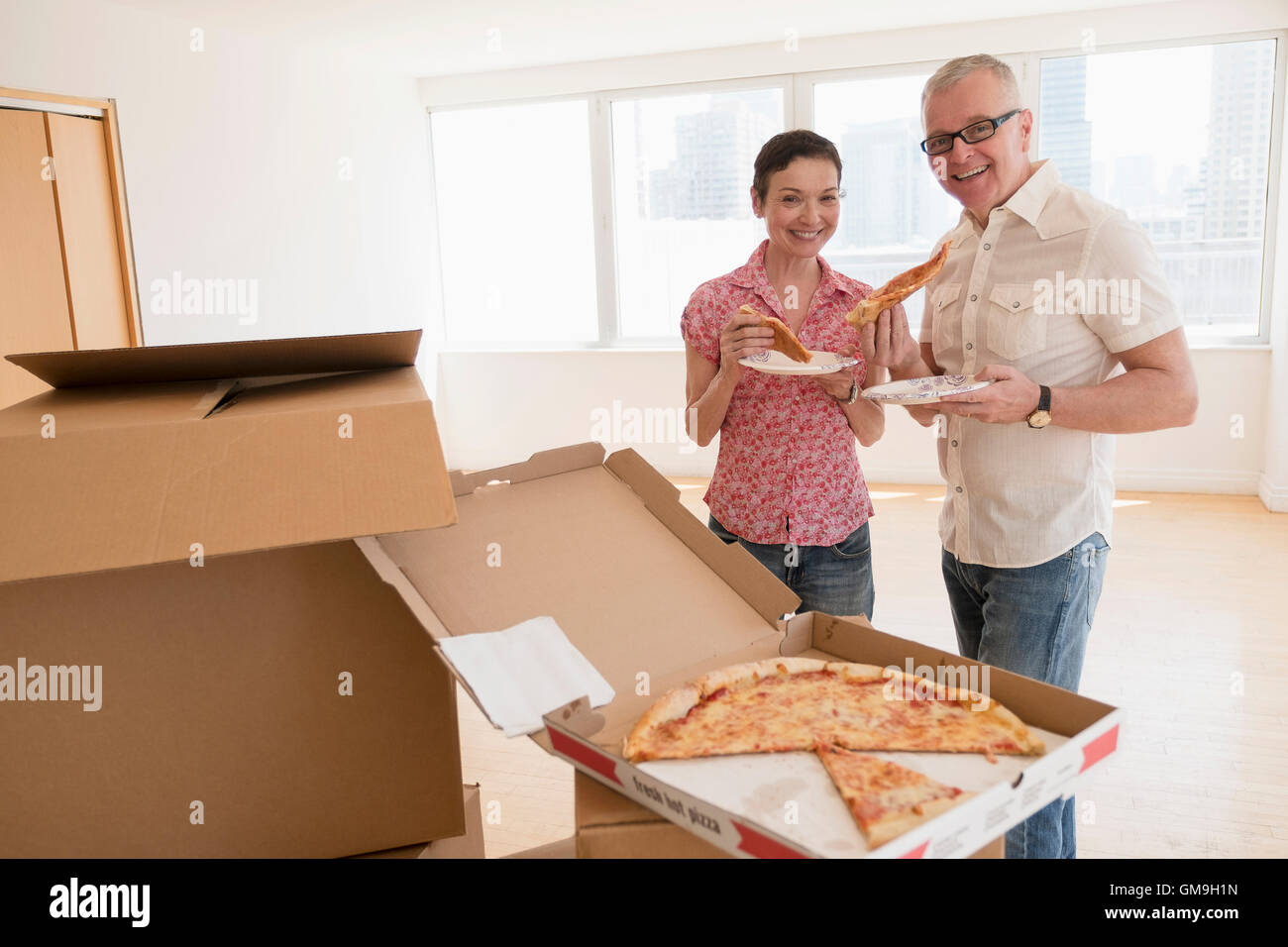 Portrait of smiling couple eating pizza in new apartment Stock Photo