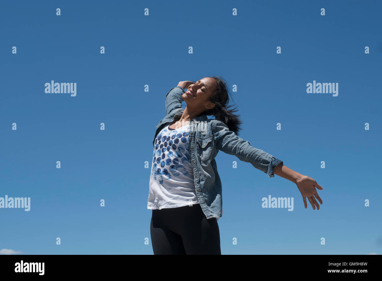 Mid adult woman outstretching her arms against blue sky Stock Photo