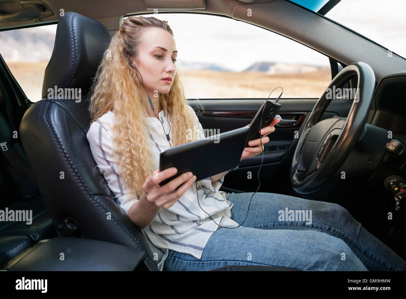 Woman sitting in car and using tablet and mobile phone at same time Stock Photo