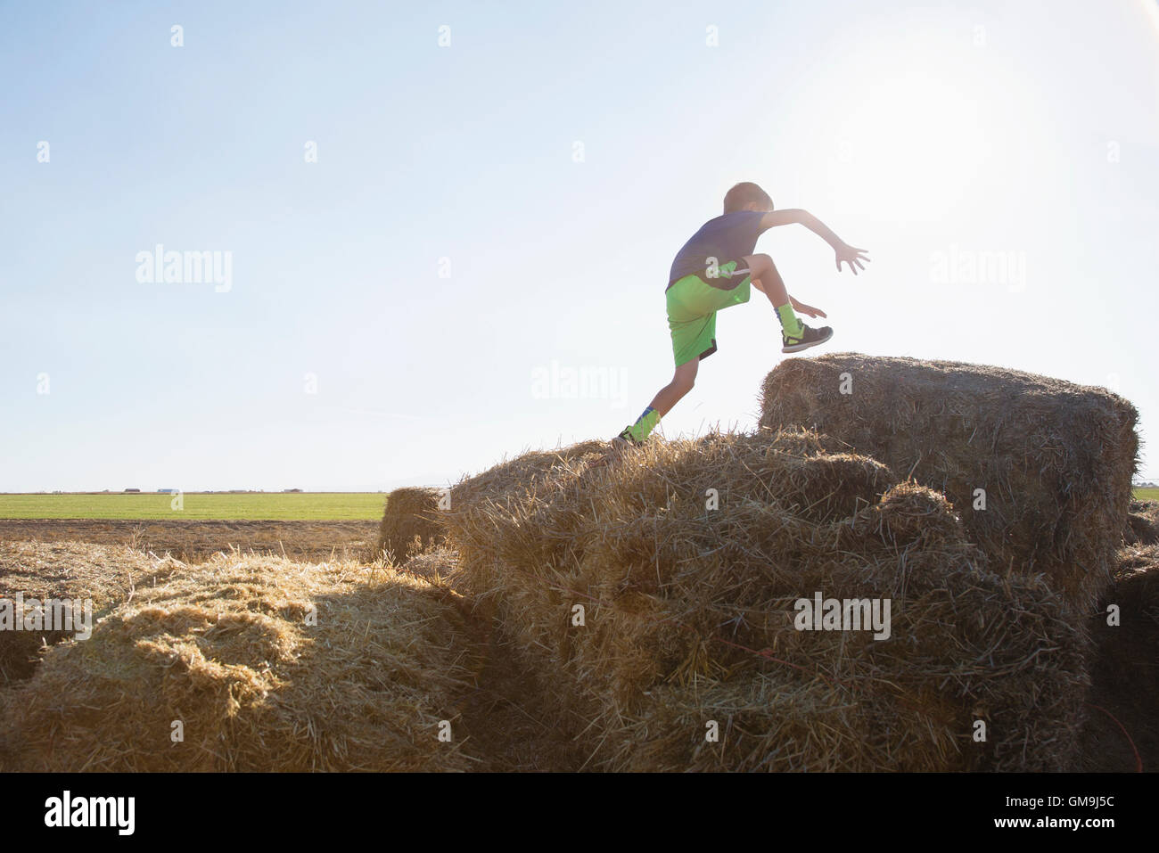 Boy (6-7) jumping on bale of hay Stock Photo