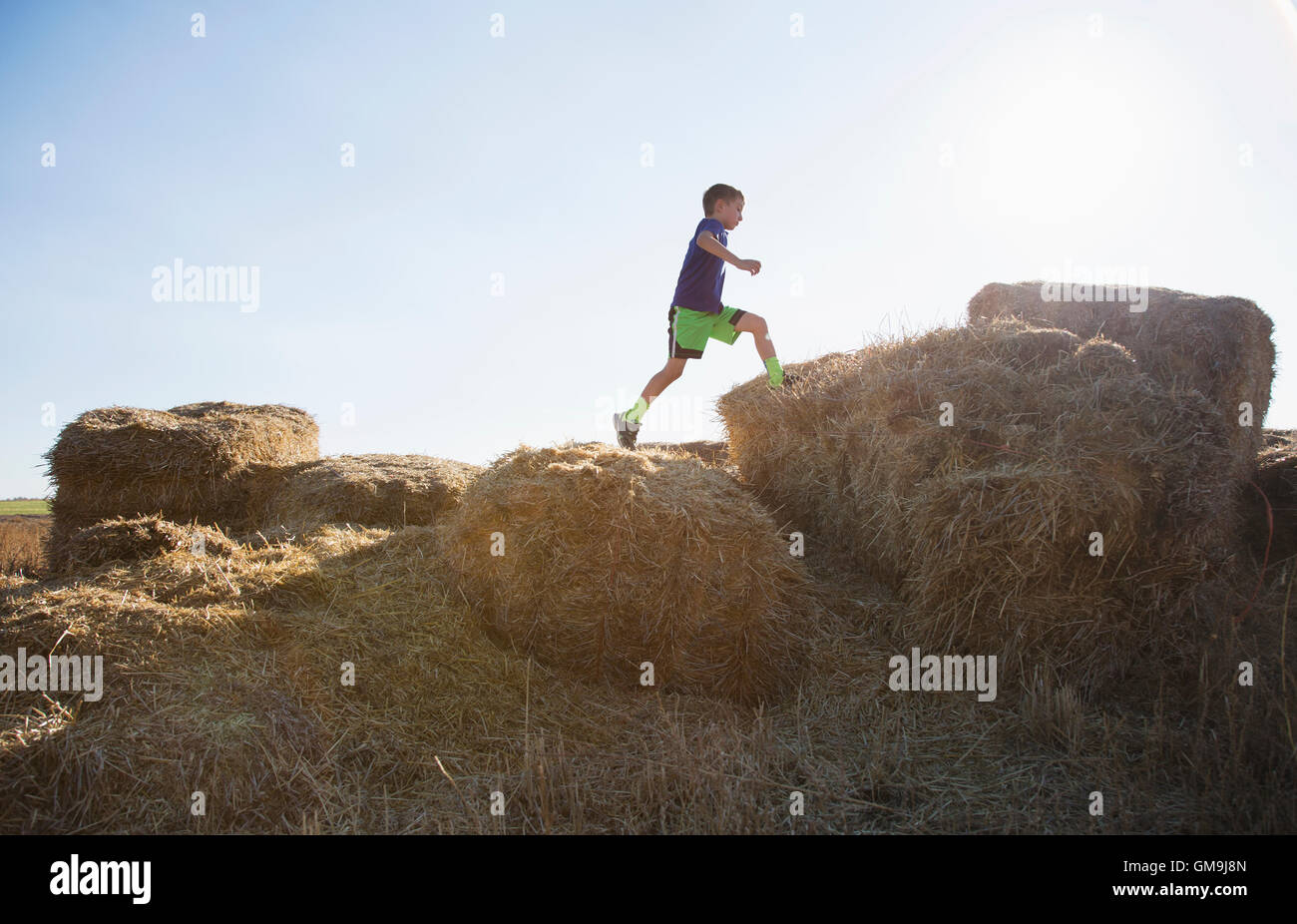 Boy (6-7) running on straw bales at sunset Stock Photo