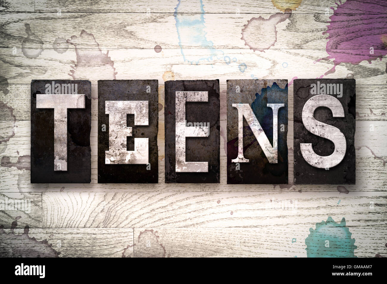 The word "TEENS" written in vintage dirty metal letterpress type on a whitewashed wooden background with ink and paint stains. Stock Photo