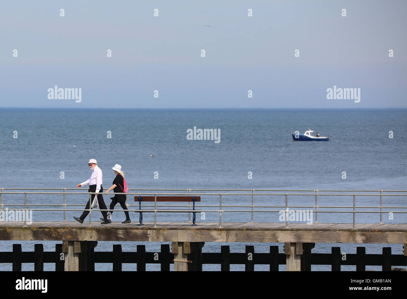 An older couple walking along a jetty on a sunny morning Stock Photo