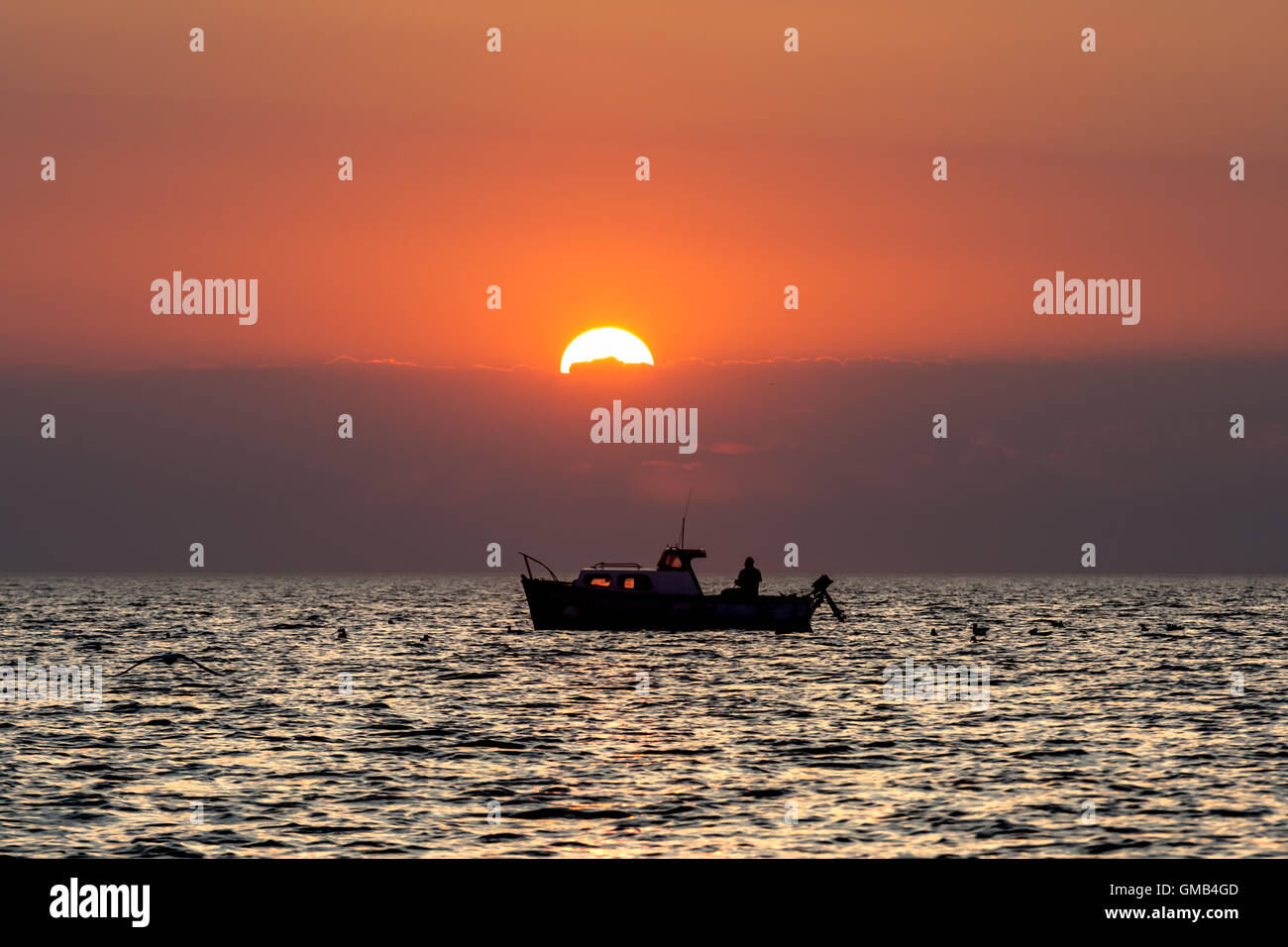 A man fishing of his boat at sunset while anchored in Cardigan bay ...