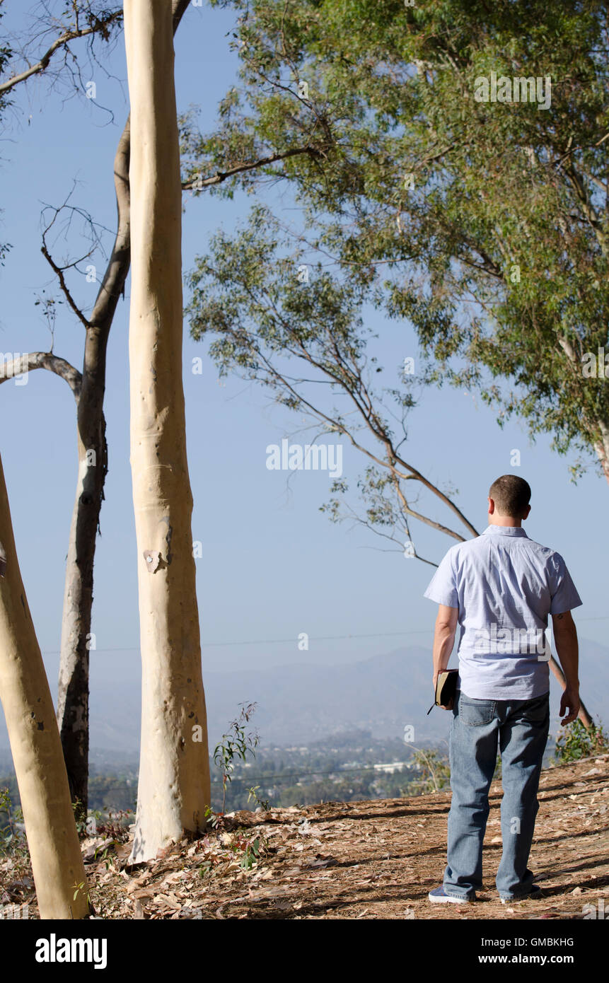 Man looking out holding a book on a hillside wearing a blue collard shirt. Stock Photo