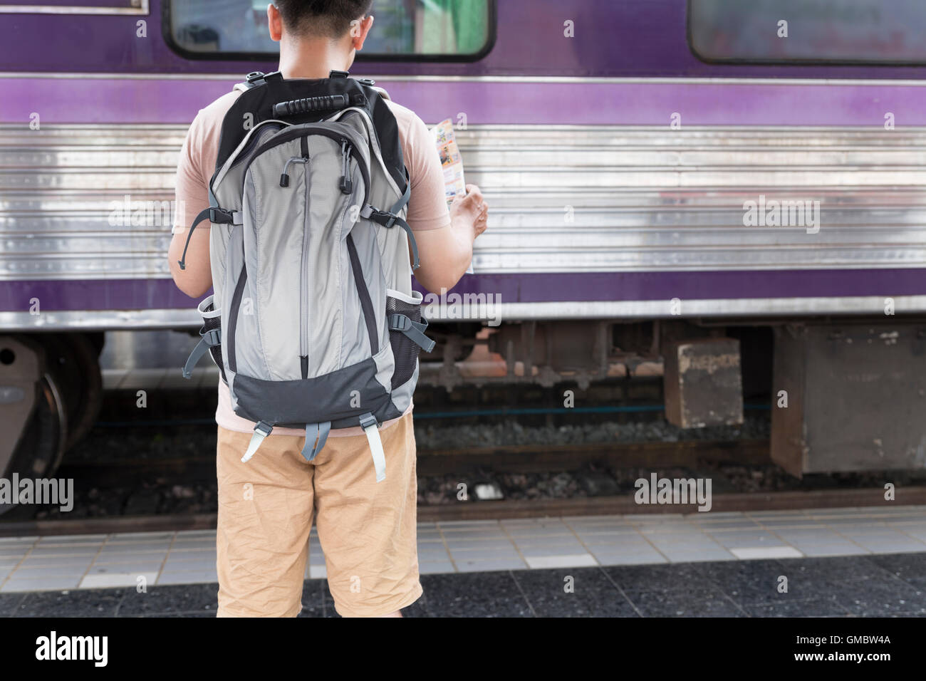 young man holding map with backpack standing on platform at train ...