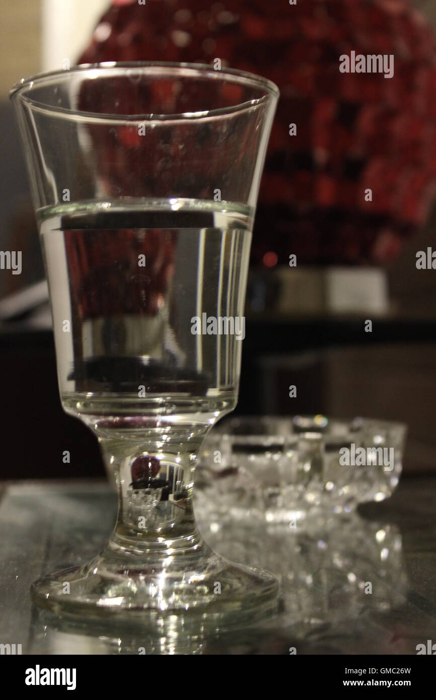 A photograph with a half filled glass of water and a red vase  which gives a pop of color to the transparent elements. Stock Photo