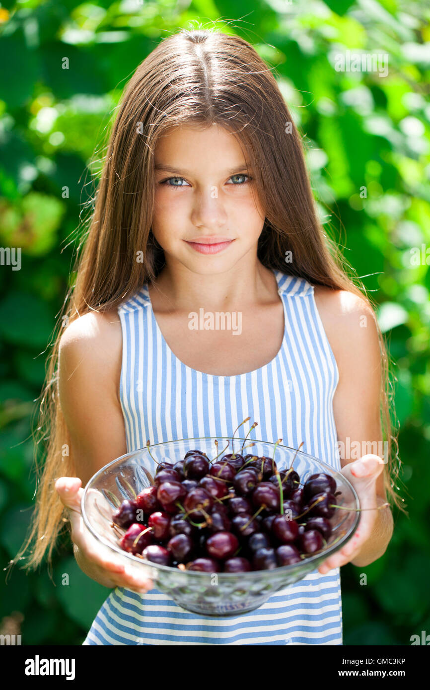 Beautiful brunette little girl holding a bowl of cherries in the garden ...