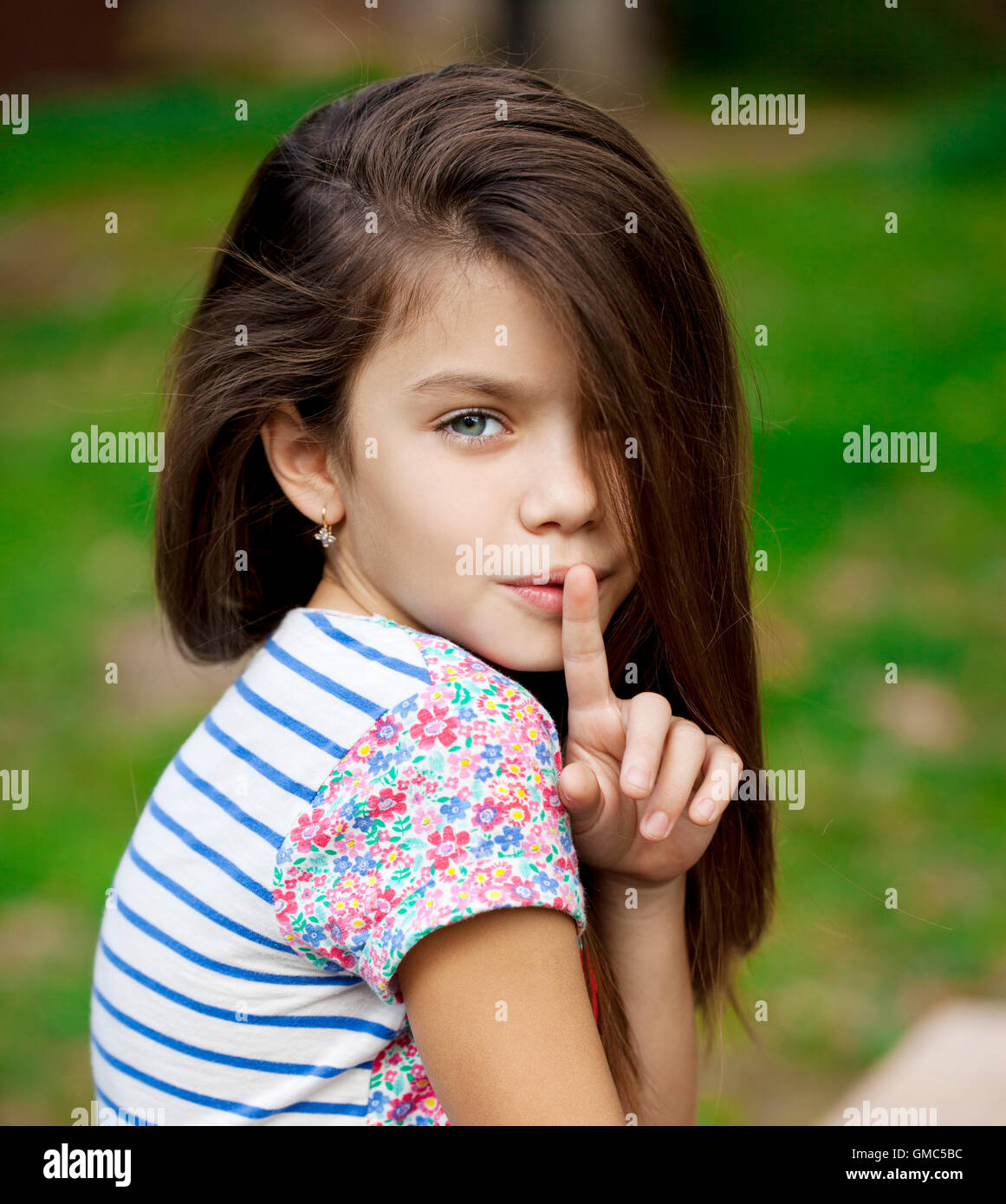 Young beautiful Little girl has put forefinger to lips as sign of silence, outdoors summer Stock Photo