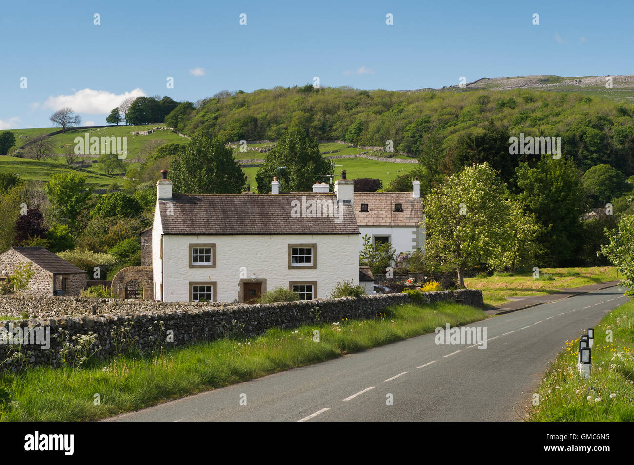 Country lane passes traditional, white, stone-built, Yorkshire Dales cottages -  Austwick village, North Yorkshire, England. Stock Photo