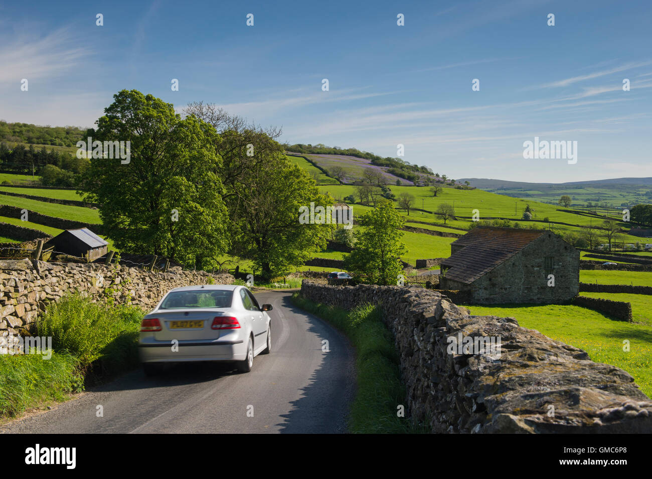 Blue sky over car driving along a narrow country lane in beautiful, scenic Crummackdale in the Yorkshire Dales, England. Stock Photo