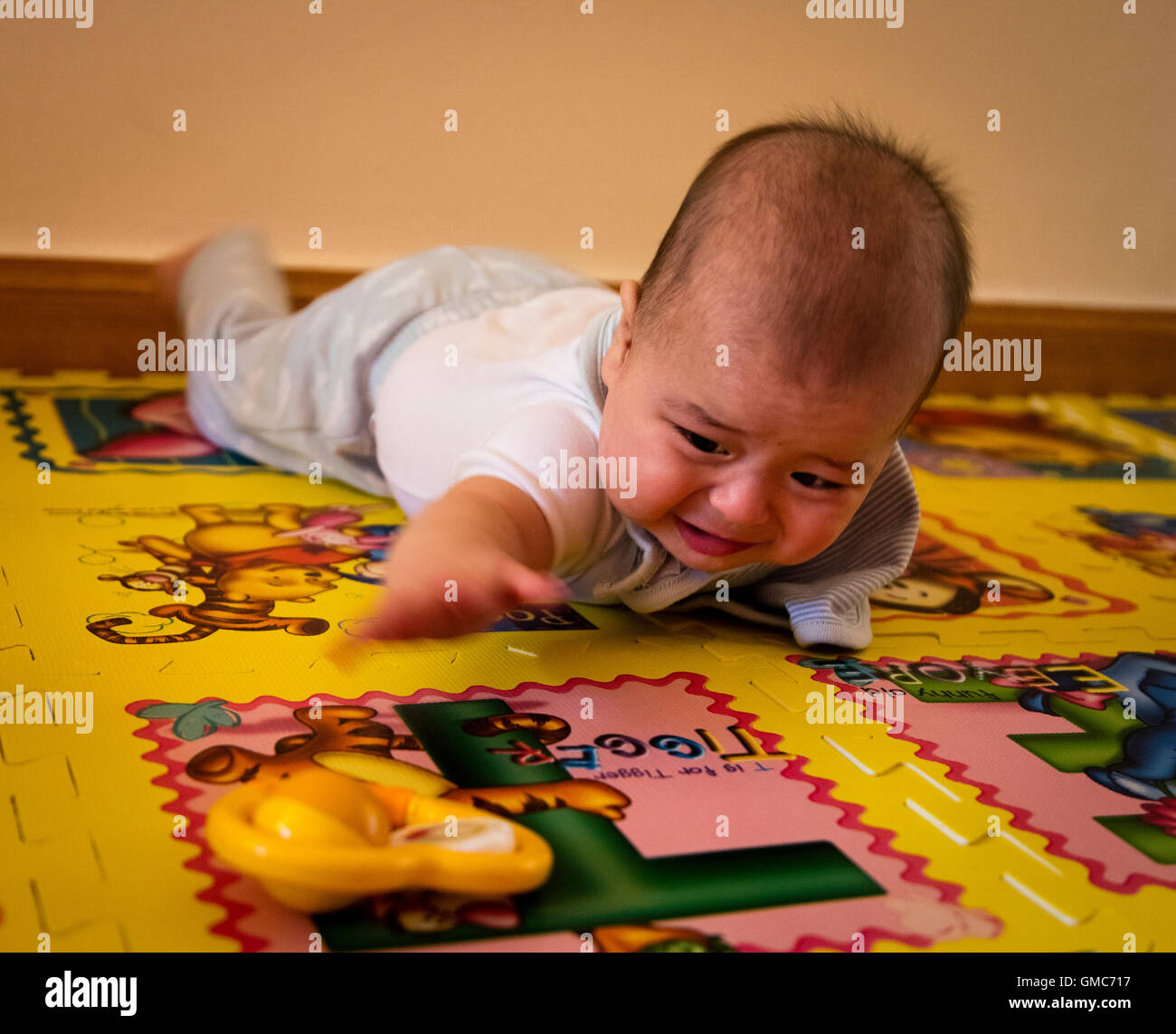 Baby stretching for toy rattle frustrated that it is out of reach Stock Photo