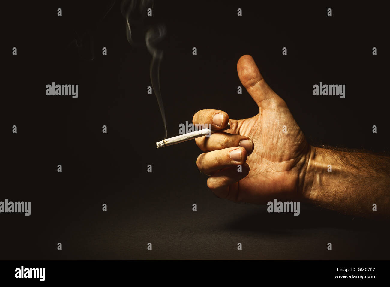 Conceptual composition about smoking, studio shot of a man's hand holding a cigar. Stock Photo