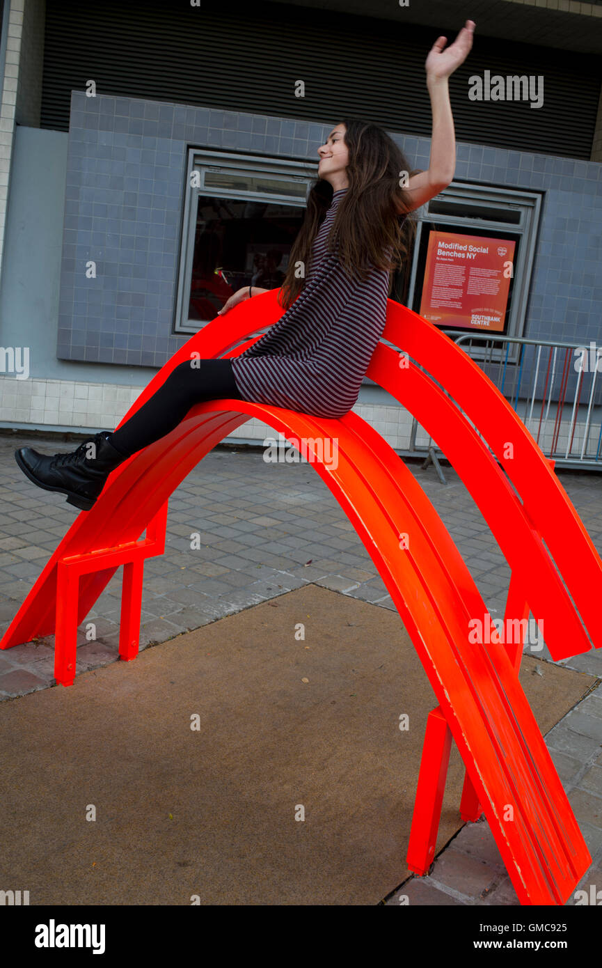 London.South Bank. Modified social bench NY. Jeppe Hein's reinvention of the park bench. Girl posing on steeply curved bench. Stock Photo