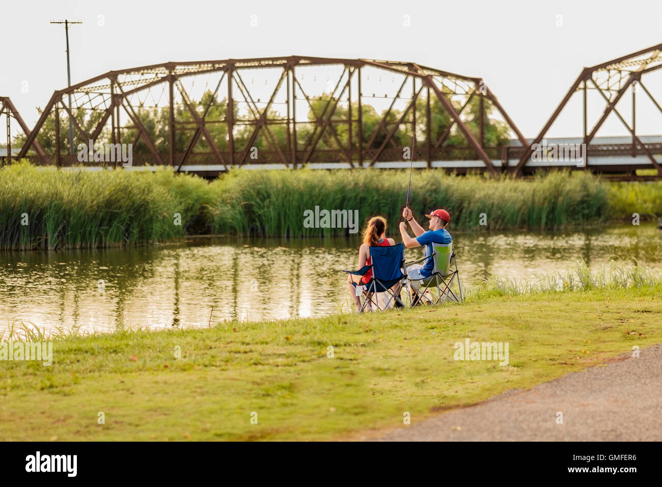 A young Caucasian couple enjoy fishing on the shoreline of the North Canadian river near the Lake Overholser steel truss bridge. Oklahoma, USA. Stock Photo