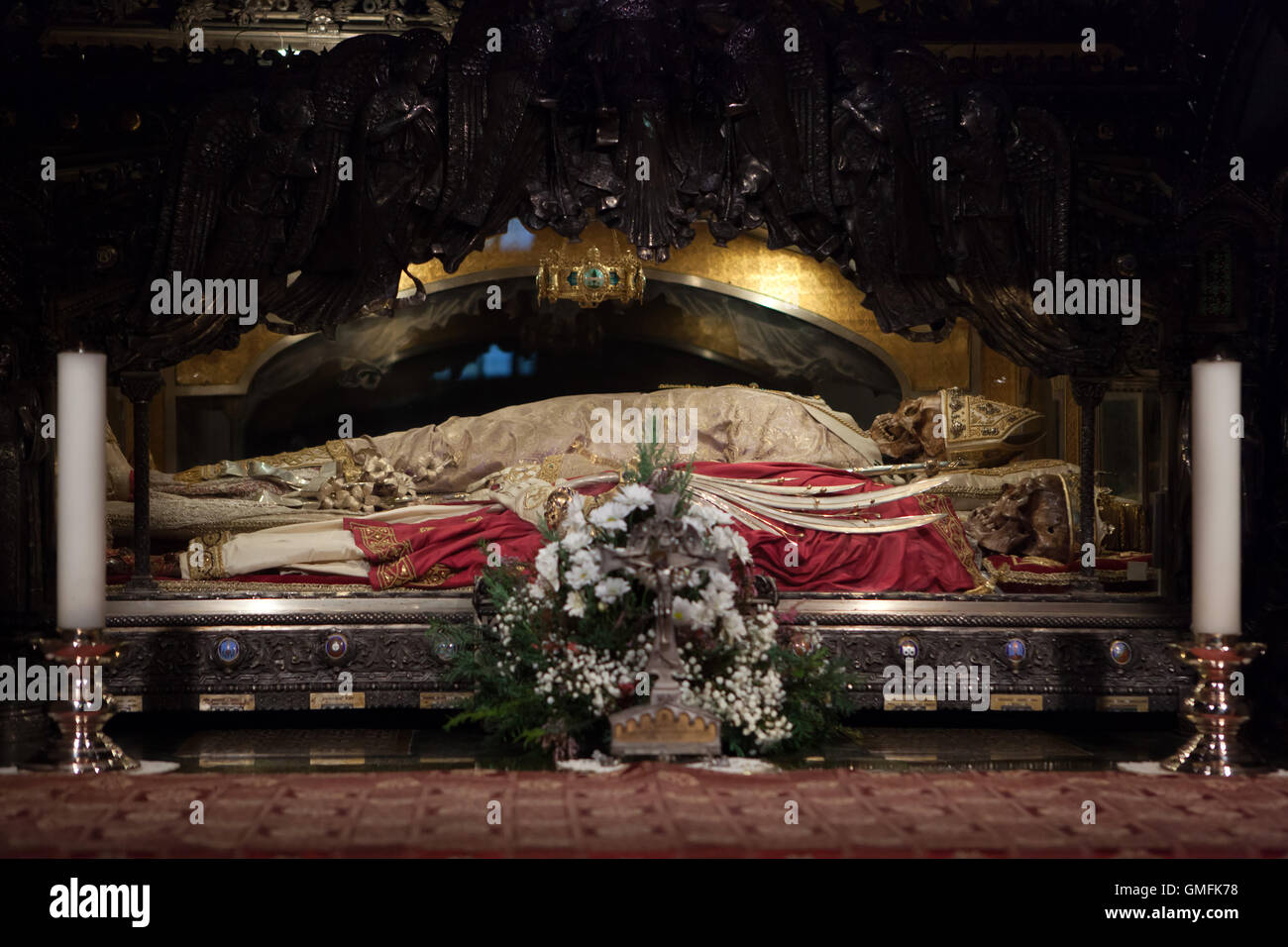 Relics of Saint Ambrose next to relics of Saints Gervasius and Protasius in the underground crypt of the Basilica di Sant'Ambrogio in Milan, Lombardy, Italy. Saints Ambrose is displayed dressed white pontifical robes while Christian martyrs Saints Gervasius and Protasius (one of them isn't visible in the picture) are displayed dressed white and gold surplices, red dalmatics and golden crowns with palm leaves as a symbol of martyrdom. The silver urn was created by Giovanni Lomazzi in 1897 after design by Ippoliti Marchetti. Stock Photo