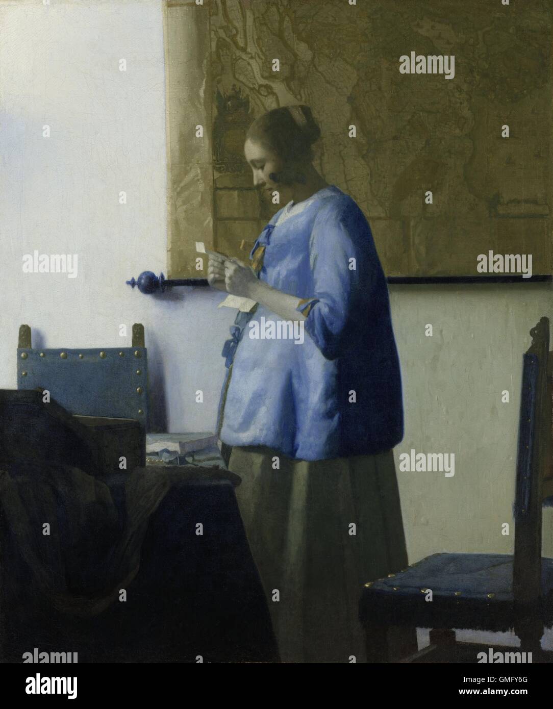 Woman Reading a Letter, by Johannes Vermeer, 1663, Dutch painting, oil on canvas. A young woman in a blue jacket, stands by a table with chairs. A large map hangs on the wall behind her (BSLOC 2016 3 1) Stock Photo
