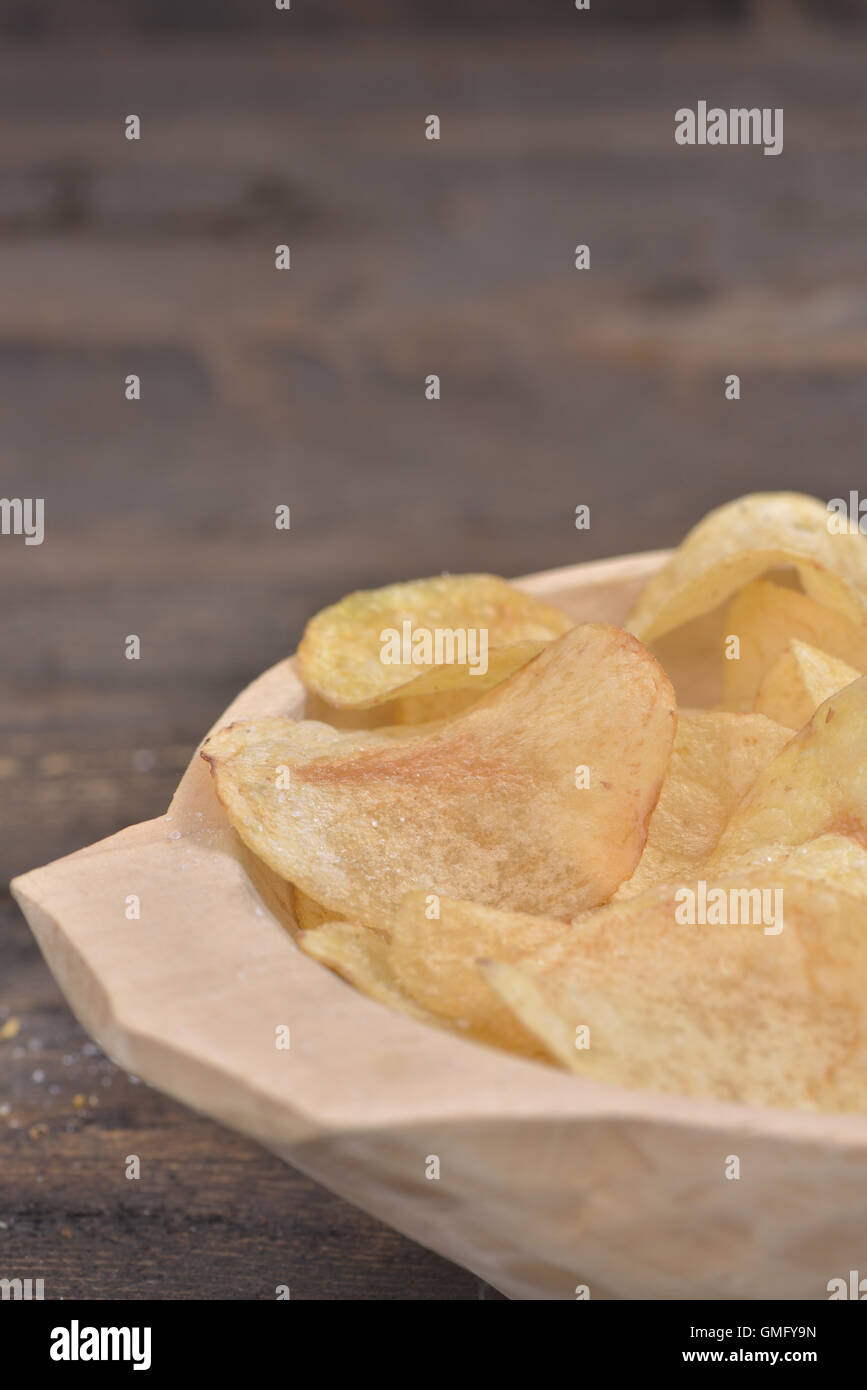 Gold salted potato chips in a wooden bowl on a rustic brown table Stock Photo