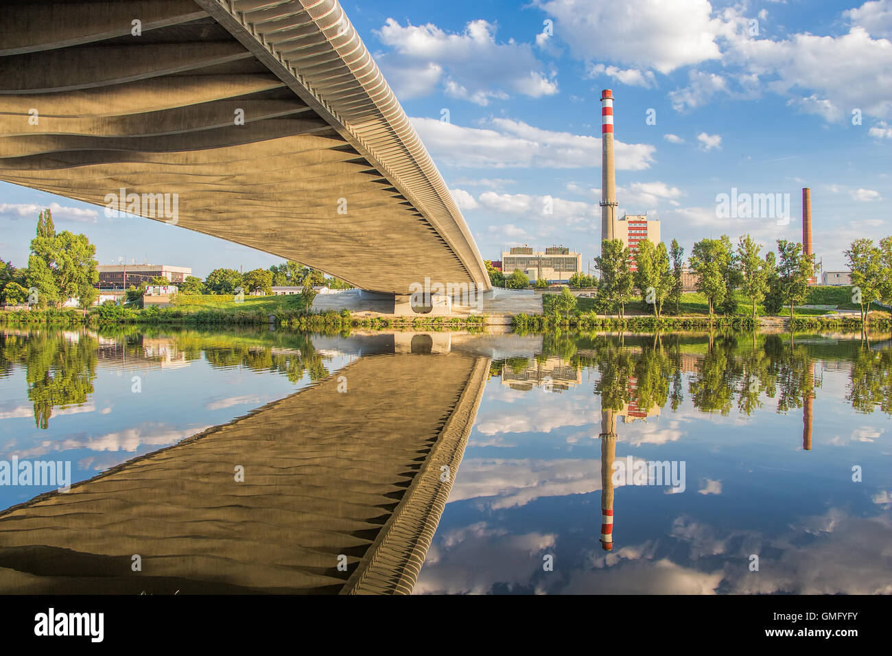 Industrial area of Prague. Chimneys, industrial buildings, clear sky, clouds, bridge with reflection on Prague river Vltava. Stock Photo