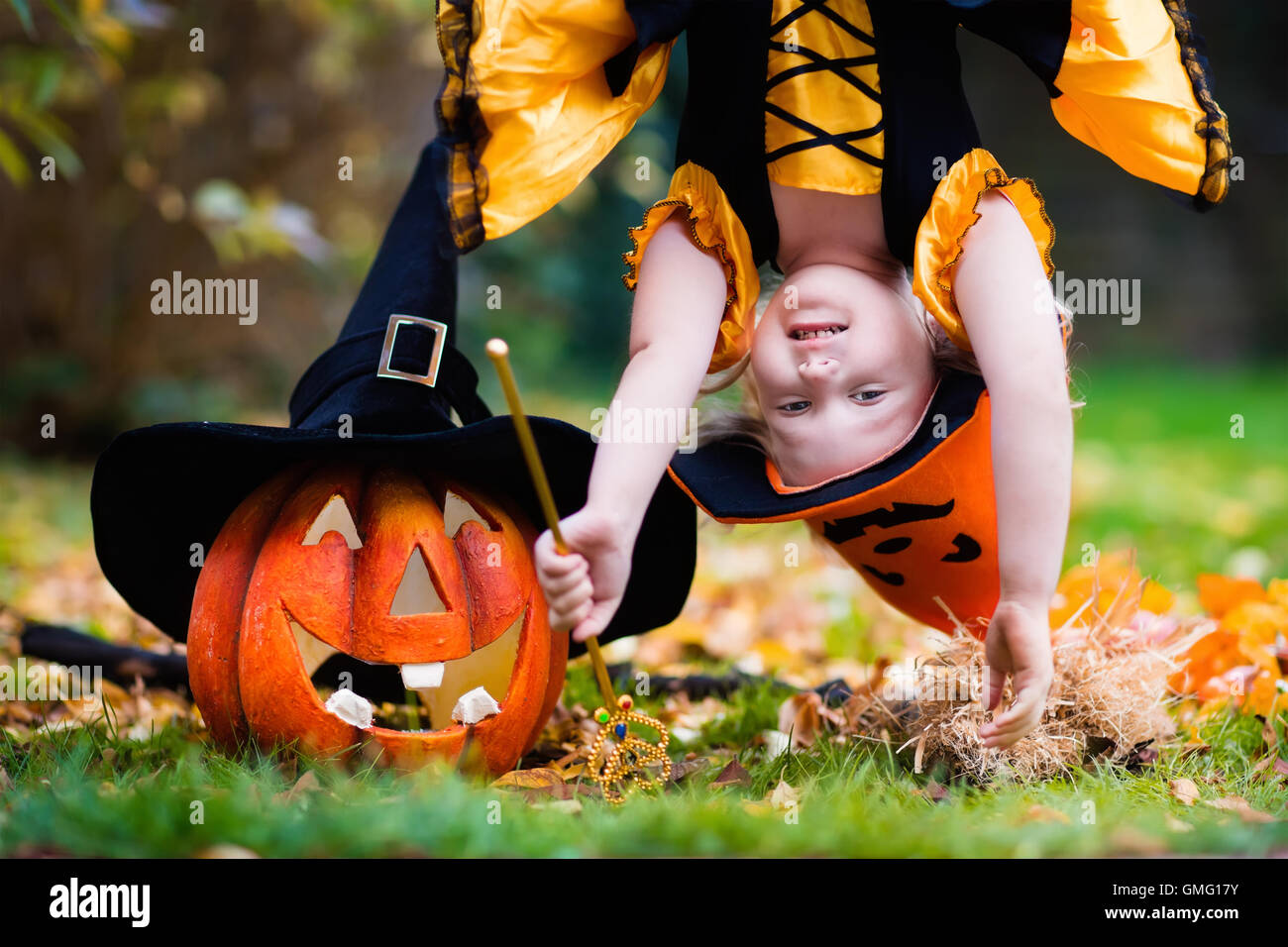 Little girl in witch costume playing in autumn park. Child having fun at Halloween trick or treat. Kids trick or treating. Stock Photo