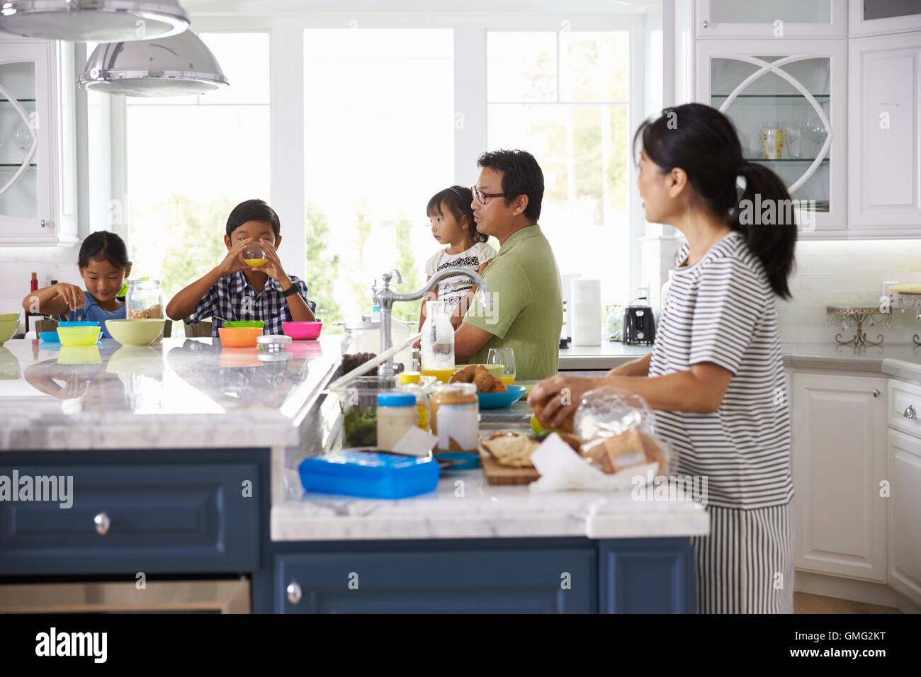Family Having Breakfast And Making Lunches In Kitchen Stock Photo