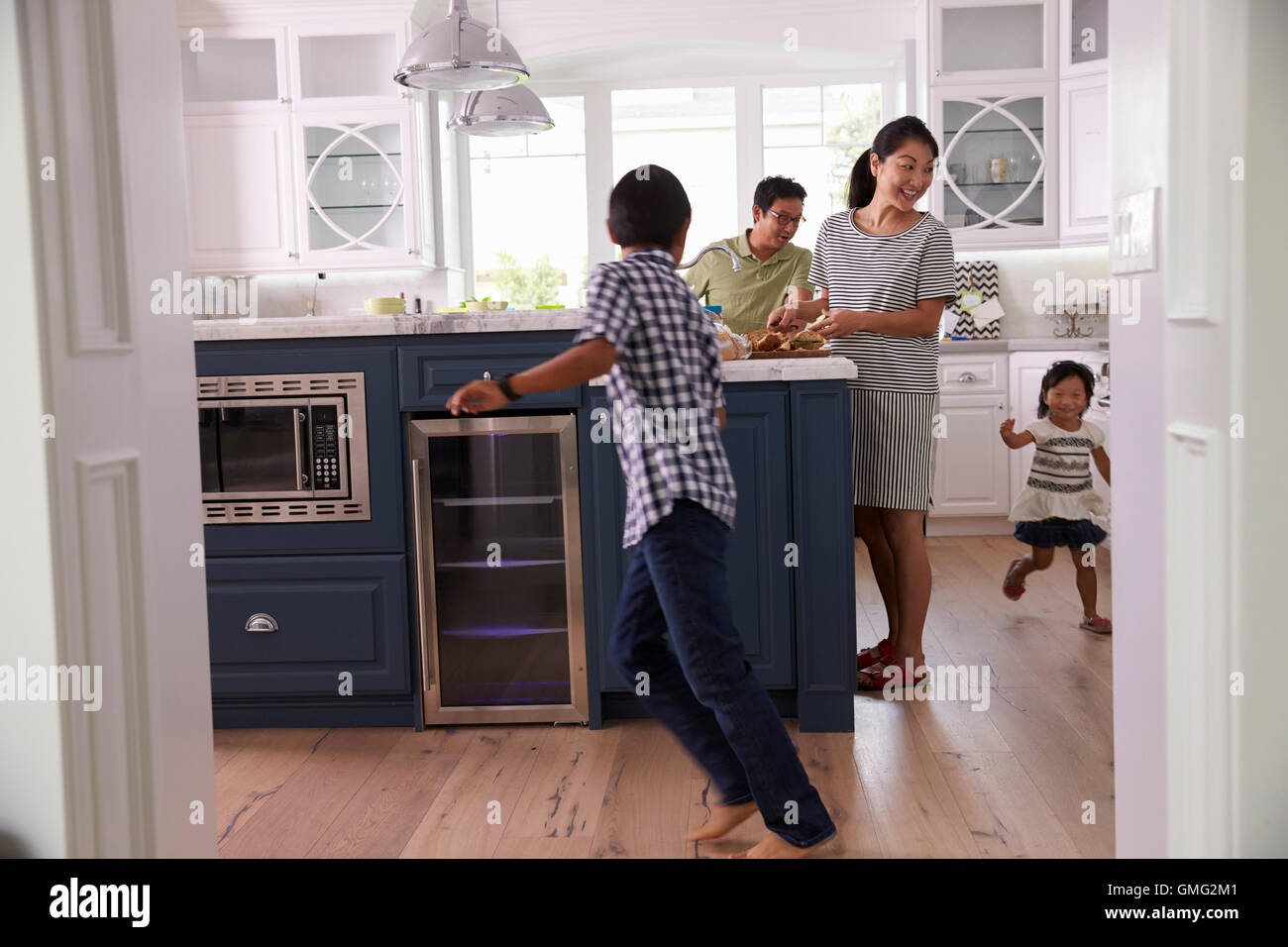 Parents Prepare Food As Children Play In Kitchen Stock Photo